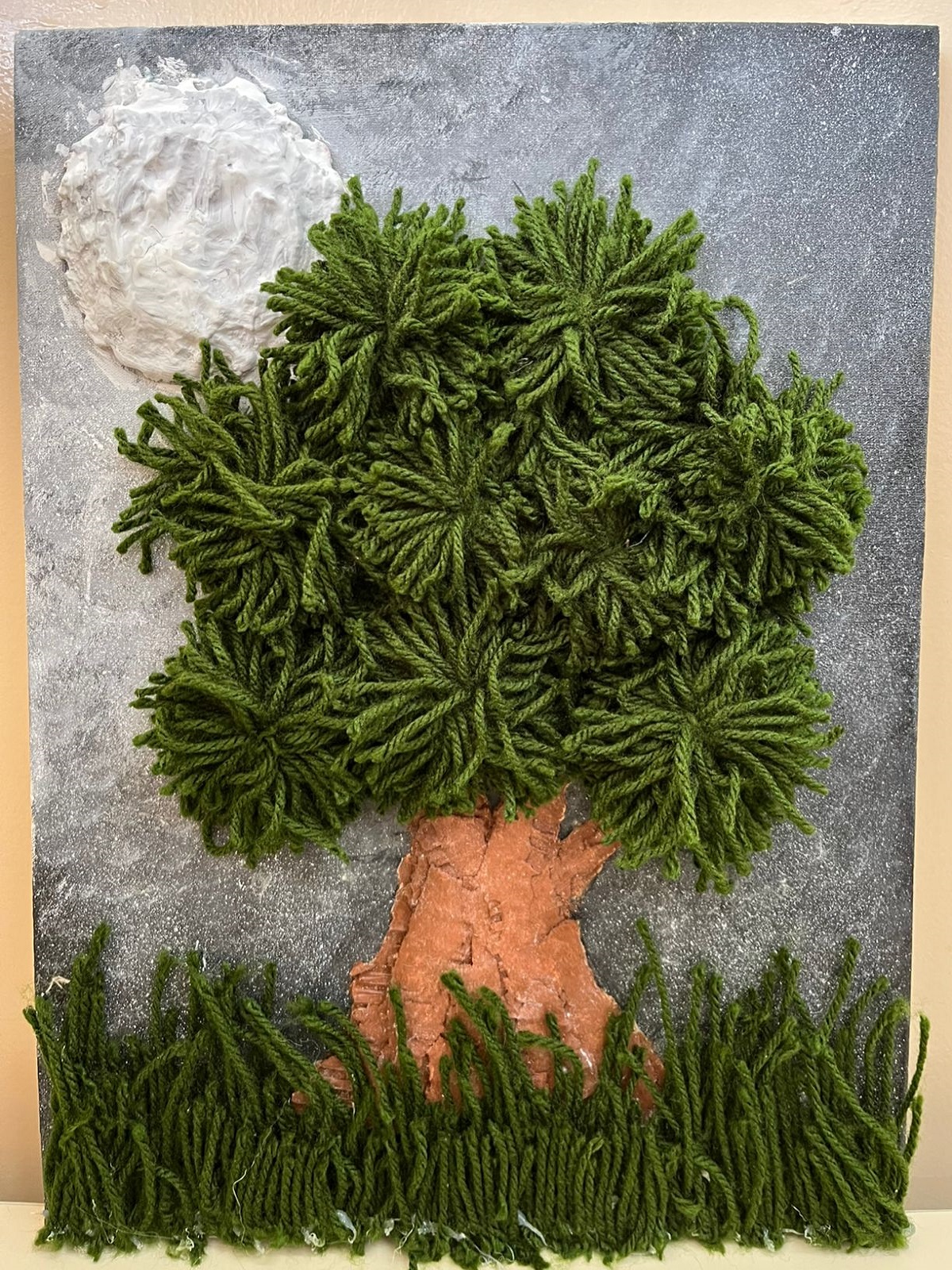 Obra em tela com árvore de lã e papelão sobre gramado verde, lua cheia de gesso e céu estrelado em degradê noturno
