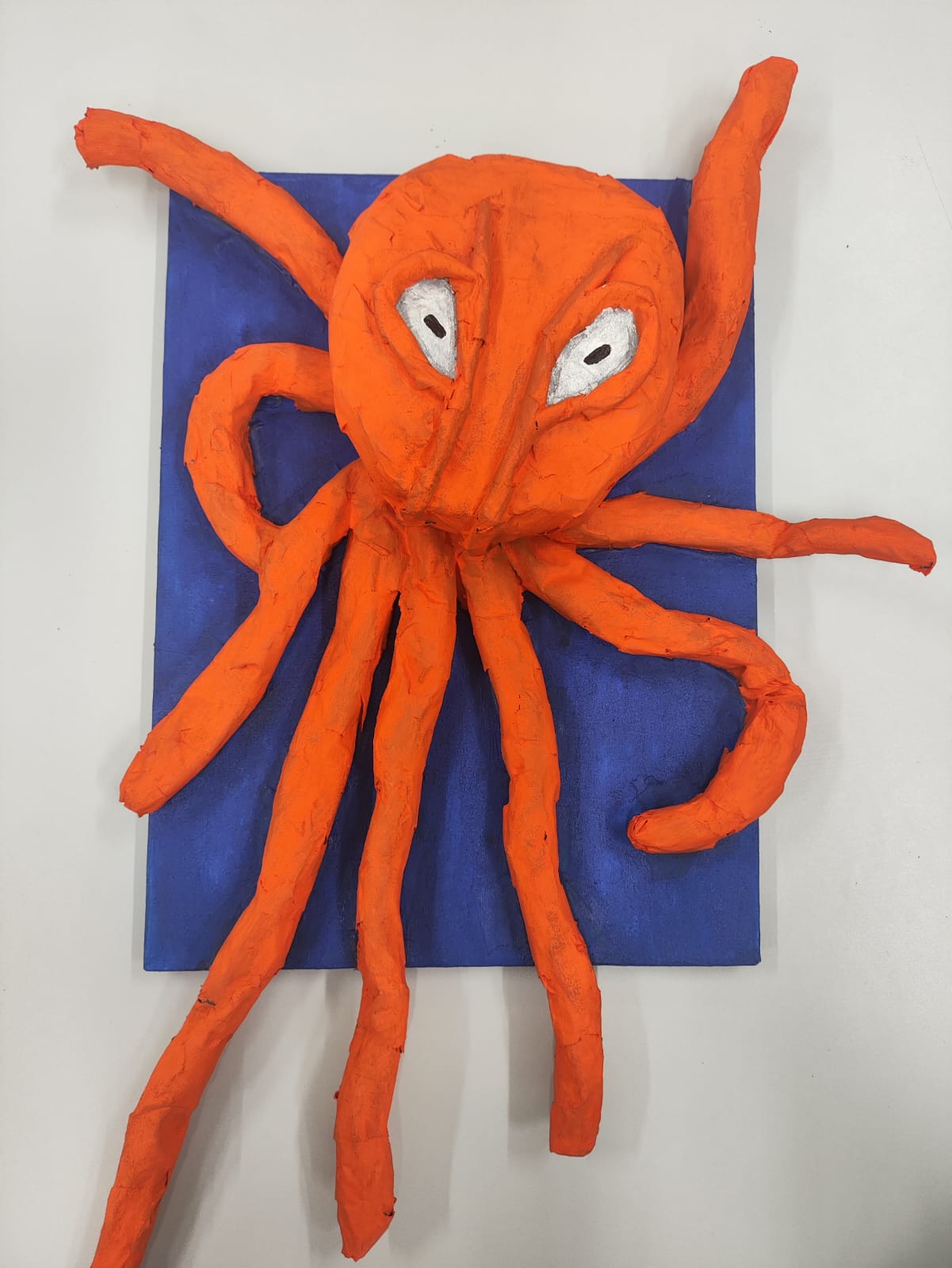  Escultura de um polvo laranja com olhos brancos em fundo azul