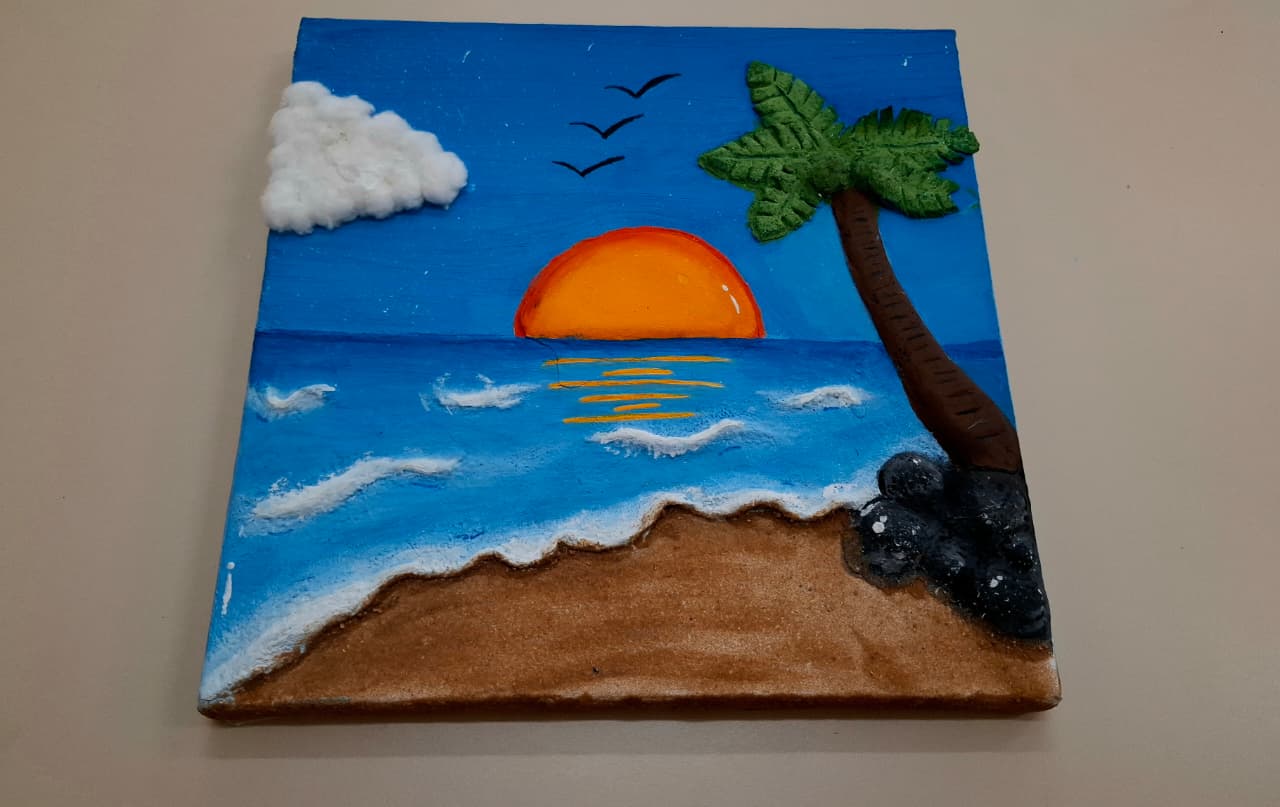  Cena em relevo com céu azul, nuvem, passarinhos, sol se pondo, mar, coqueiro e pedras.