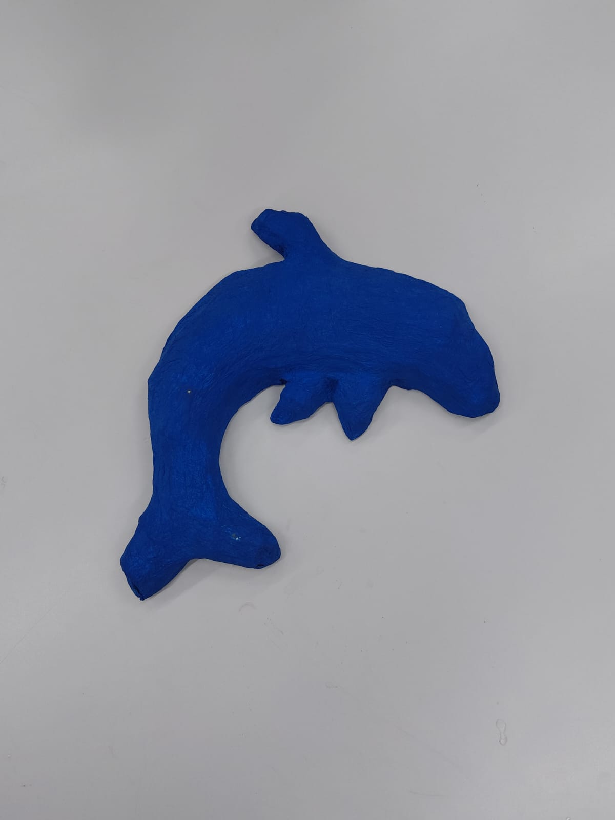 A obra retrata um golfinho em movimento, feito com papelão, cola e tinta guache azul