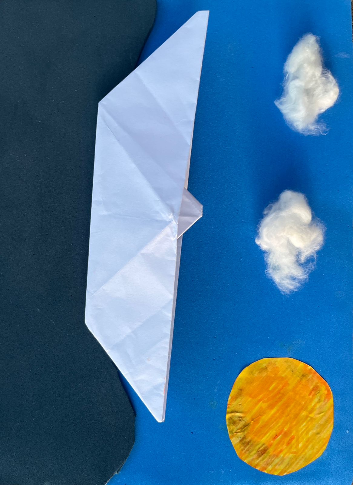 Barquinho de papel sobre o oceano, com sol no canto superior esquerdo e nuvens de algodão acima